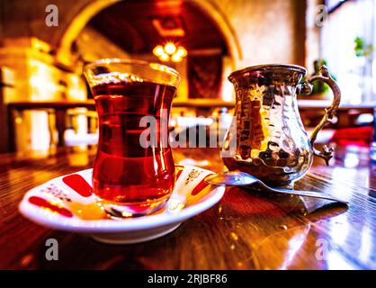 Tazza di tè nero in vetro con teiera con foglie di tè fresco, bevanda calda tradizionale turca Foto Stock