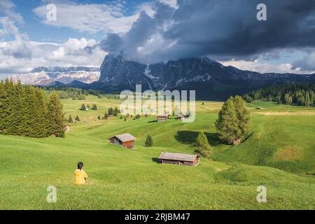 Dolomiti d'Italia in primavera, Una donna siede sul prato dell'Alpe di Siusi godendo del paesaggio naturale di prati, fiori e montagne Foto Stock