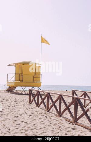 Yellow lifeguard tower or station at a beach with a yellow flag.  All words and lettering removed from the structure Stock Photo