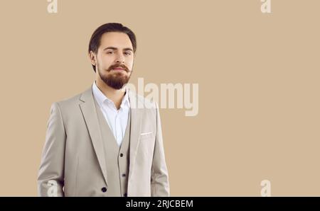Uomo giovane sicuro ed elegante che guarda la fotocamera con un look sicuro su sfondo beige. Foto Stock