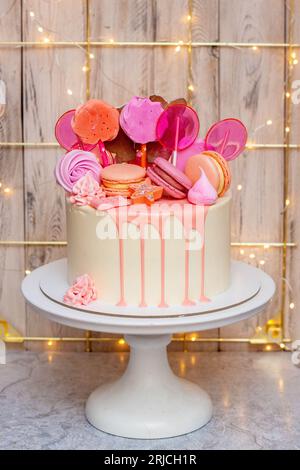 Torta bianca con cioccolato fuso rosa, meringhe e lecca lecca su sfondo festivo Foto Stock