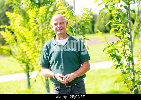 Ellerhoop, Germania. 22 agosto 2023. Andreas Wrede, responsabile delle sperimentazioni di vivaio presso il Centro orticolo della camera di Agricoltura di Ellerhoop, si trova tra varie varietà di olmo in fase di ricerca per un esemplare adatto al vivaio che può essere prodotto economicamente e in modo sensibile al clima. Quali alberi possono resistere all'avanzamento del cambiamento climatico nelle nostre città? Martedì gli esperti hanno cercato soluzioni in un simposio nel centro vivaistico Ellerhoop (distretto di Pinneberg). Crediti: Jonas Walzberg/dpa/Alamy Live News Foto Stock