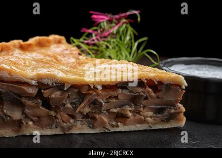 un pezzo di torta di quiche al forno, con funghi e salsa, primo piano, su sfondo nero Foto Stock