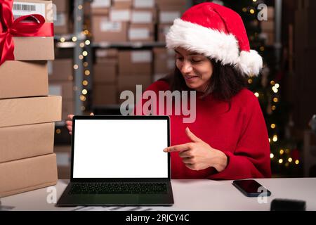 Responsabile del magazzino che utilizza un computer portatile con spazio vuoto per il mock-up e punta il dito su di esso, saldi natalizi, spazio per la pubblicità Foto Stock