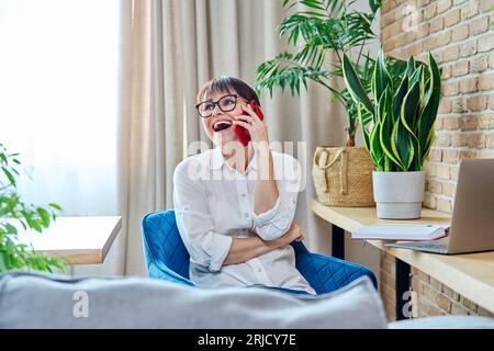 Felice donna di mezza età che parla al cellulare, a casa Foto Stock