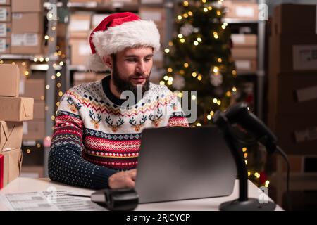 Affari di consegna di Natale. Addetto al magazzino che prepara i pacchi utilizzando un software portatile nel magazzino. PMI, vendita online Foto Stock