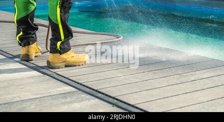Uomo che pulisce il suo ponte a bordo piscina con acqua. Manutenzione dell'area della piscina. Foto Stock