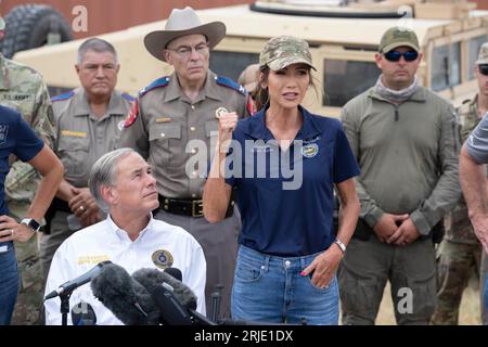 Il governatore del Dakota del Sud KRISTI NOEM si rivolge alla stampa mentre il governatore del Texas GREG ABBOTT (a sinistra) ascolta mentre diversi governatori degli Stati Uniti tengono un briefing lungo il Rio grande a Eagle Pass, Texas, il 21 agosto 2023. I governatori hanno fatto un tour in elicottero del fiume dove una controversa serie di boe di oltre mille metri sono state collocate per scoraggiare i migranti dall'attraversamento. Foto Stock