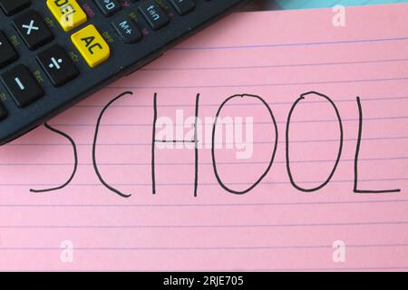 Una foto della parola "Scuola" scritta su una flashcard rosa con un pennarello nero e una calcolatrice accanto. Foto Stock