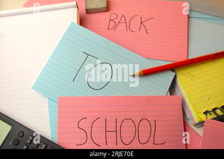 Una foto delle parole "Back to School" scritte su flashcard colorate su una scrivania con calcolatrici, gomme e cartelle. Foto Stock