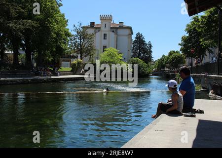 Father and son relax by the banks of the River Sorgue on a warm spring day in  L'Isle sur la Sorgue. Concept for locals relaxing, tourists cooling off Stock Photo