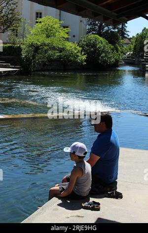 Padre e figlio si rilassano sulle rive del fiume Sorgue in una calda giornata primaverile a l'Isle sur la Sorgue. Ideale per il relax della gente del posto e per il relax dei turisti Foto Stock