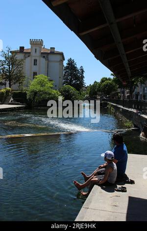 Padre e figlio si rilassano sulle rive del fiume Sorgue in una calda giornata primaverile a l'Isle sur la Sorgue. Ideale per il relax della gente del posto e per il relax dei turisti Foto Stock