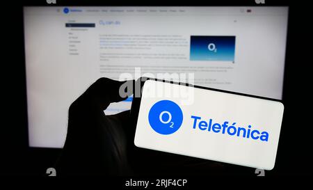 Persona che possiede il cellulare con il logo della società telefonica Deutschland Holding AG sullo schermo davanti alla pagina Web dell'azienda. Concentrarsi sul display del telefono. Foto Stock