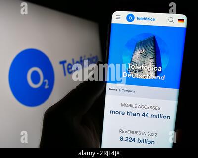 Person holding cellphone with webpage of company Telefonica Deutschland Holding AG on screen in front of logo. Focus on center of phone display. Stock Photo