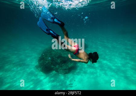 Corpo completo di giovane subacqueo anonimo con maschera da snorkeling e pinne che nuotano sott'acqua ed esplorano la barriera corallina e l'ecosistema del fondo marino Foto Stock