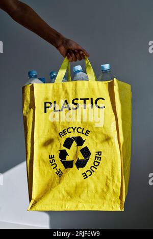 Coltivare volontaria donna anonima che tiene un sacchetto giallo con bottiglie di plastica scelte per il riciclaggio e l'ambiente di pulizia dalla spazzatura Foto Stock