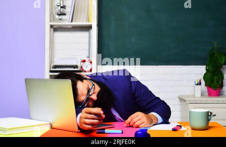 Torna a scuola. Lavoro scolastico. Giornata degli insegnanti. Insegnante maschio stanco con gli occhiali che dorme alla scrivania in classe. Pausa scolastica. Un'università universitaria piena di lavoro Foto Stock