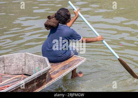 Una donna siede sulla prua di una barca e sta pagaiando con una pagaia, Thailandia Foto Stock