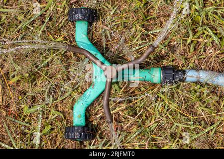 L'irrigatore da giardino ruota e spruzza acqua sull'erba Foto Stock