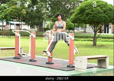 Bella donna asiatica che fa esercizio sportivo con un tipo di macchina per esercizi che oscilla le gambe nel parco all'aperto. Foto Stock