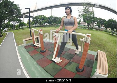 Bella donna asiatica che fa esercizio sportivo con un tipo di macchina per esercizi che oscilla le gambe nel parco all'aperto. Foto Stock