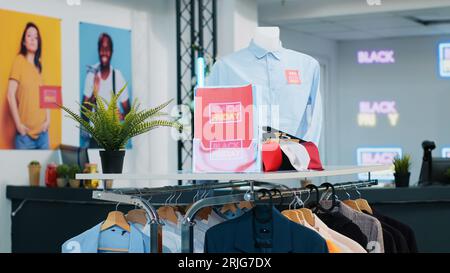 Etichette di vendita stagionali nel negozio di abbigliamento, cartellini di prezzo rossi sul merchandising che indicano le promozioni. Attira i clienti ad acquistare abiti di vari marchi durante l'evento del Black friday presso i grandi magazzini. Foto Stock