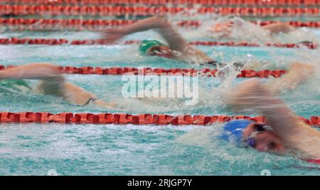Un'immagine volutamente sfocata di più nuotatori freestyle che gareggiano e competono in una piscina con corde rosse. Azione sfocata con schizzi e movimenti. Foto Stock