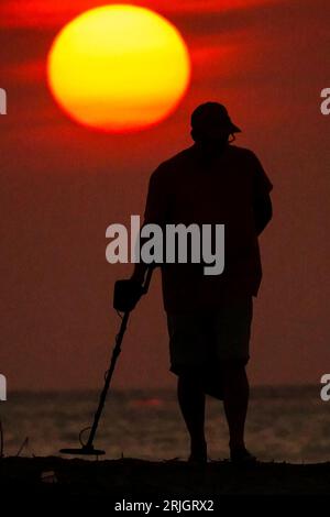 Isola di Palms, Stati Uniti. 22 agosto 2023. Un uomo sagomato dall'alba utilizza un metal detector come cupola di calore in tutto il sud porta il clima caldo e umido nella zona di Charleston, il 22 agosto 2023 a Isle of Palms, South Carolina. Crediti: Richard Ellis/Richard Ellis/Alamy Live News Foto Stock