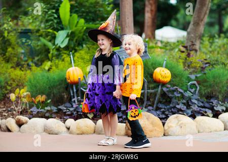 Bambino in costume di Halloween. Trucchi o delizia per i bambini. Bambino e ragazza vestita come strega con cappello che tiene lanterna di zucca e secchio di caramelle. Foto Stock