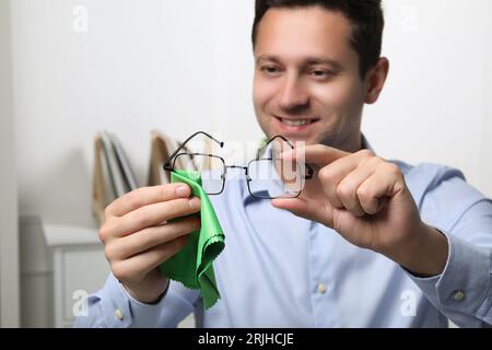 Happy MAN pulisce gli occhiali con un panno in microfibra per interni, messa a fuoco selettiva Foto Stock