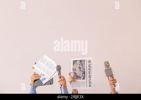 Mani femminili con giornali e microfoni su sfondo chiaro Foto Stock