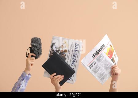 Mani femminili con microfono, notebook e giornali su sfondo a colori Foto Stock