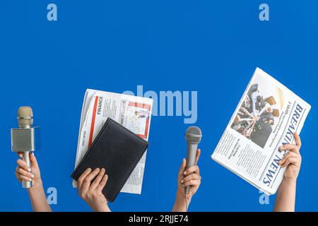 Mani femminili con giornali, microfoni e notebook su sfondo blu Foto Stock