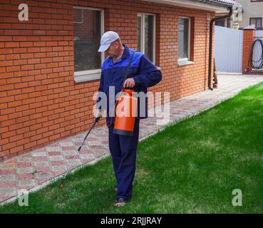 Un uomo lavora in giardino, spruzzando le erbacce da uno spruzzatore. Foto Stock