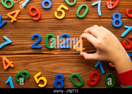 Il bambino compone l'anno 2024 da numeri multicolori su uno sfondo di legno Foto Stock