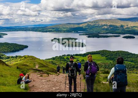 Escursionisti e escursionisti che scendono da Conic Hill con vista su Balmaha e Loch Lomond nelle Highlands scozzesi. Foto Stock