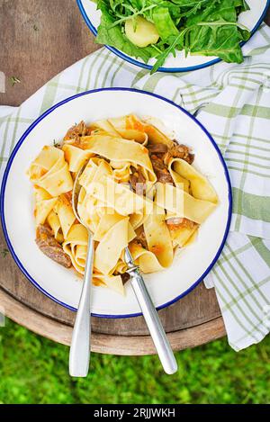 Spaghetti con tagliatelle di pasta con salsa cremosa serviti al piatto all'aperto nelle giornate di sole. Mangiare fettucine fresche o pappardelle con carne in salsa cremosa. Foto Stock
