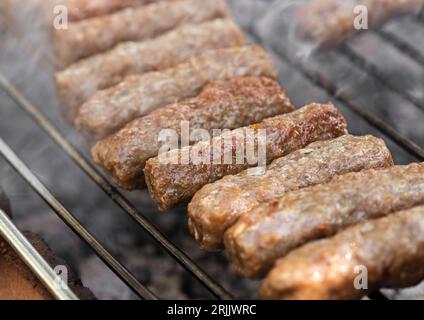 Grilling in barbecue of traditional south european skinless sausages cevapcici made of ground meat and spices outside in fireplace Stock Photo