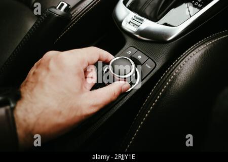 La mano del conducente sta ruotando il pulsante dell'autoradio, la mano umana regola un interruttore a pulsante sul cruscotto dei pulsanti in un'auto, concetto di parti automobilistiche. Foto Stock