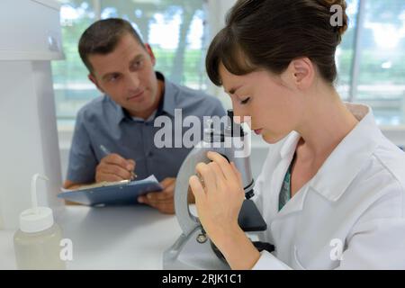 la giovane e bella assistente di laboratorio guarda al microscopio Foto Stock