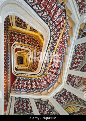 Abstract shape luxurious stairs with red carpet cover and golden handrail. Hypnotic pattern swirl staircase with mirror reflections on the stairwell w Stock Photo