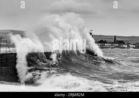 Enormi onde si infrangono nel porto di Newlyn, alcune delle quali raggiungono l'altezza e sopra il faro che si trova sulla parete del porto. Newlyn, Cornovaglia, Regno Unito Foto Stock