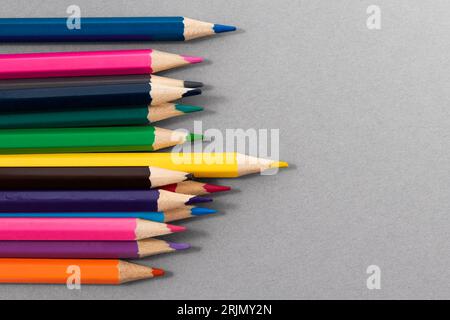 Colored pencils on gray paper with space to write to the right. Top view. Standing Out From The Crowd concept. Focus on yellow pencil in foreground. Stock Photo