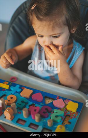 Ritratto lifestyle di una bambina che gioca con figure in legno, impara forme e colori. Concetto educativo. Blocco di legno colorato geometrico Foto Stock