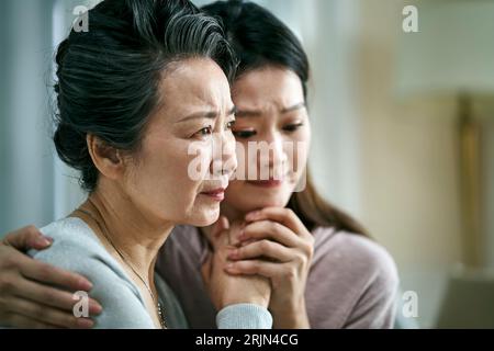 madre asiatica anziana e figlia adulta in lutto che si tengono per mano Foto Stock