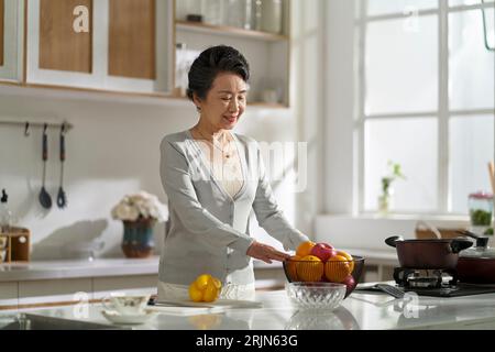 donna asiatica anziana in piedi in cucina moderna a casa preparandosi a preparare il cibo Foto Stock