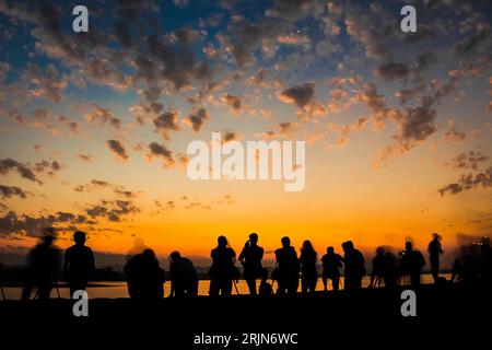 Un'immagine a lunga esposizione di un tramonto vibrante illumina un paesaggio sereno con un gruppo di persone che si stagliano contro l'orizzonte Foto Stock
