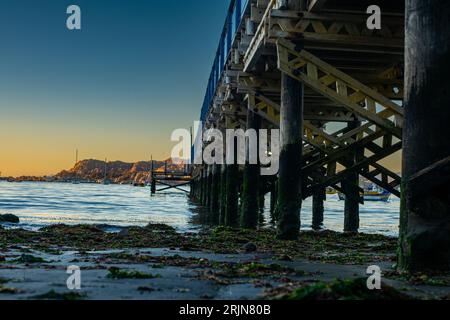 Un molo di legno con alti pali su entrambi i lati della struttura, che si estende in un mare tranquillo Foto Stock