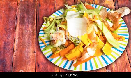 Un piatto con una varietà di bucce di verdure, seduto su un tavolo di legno Foto Stock
